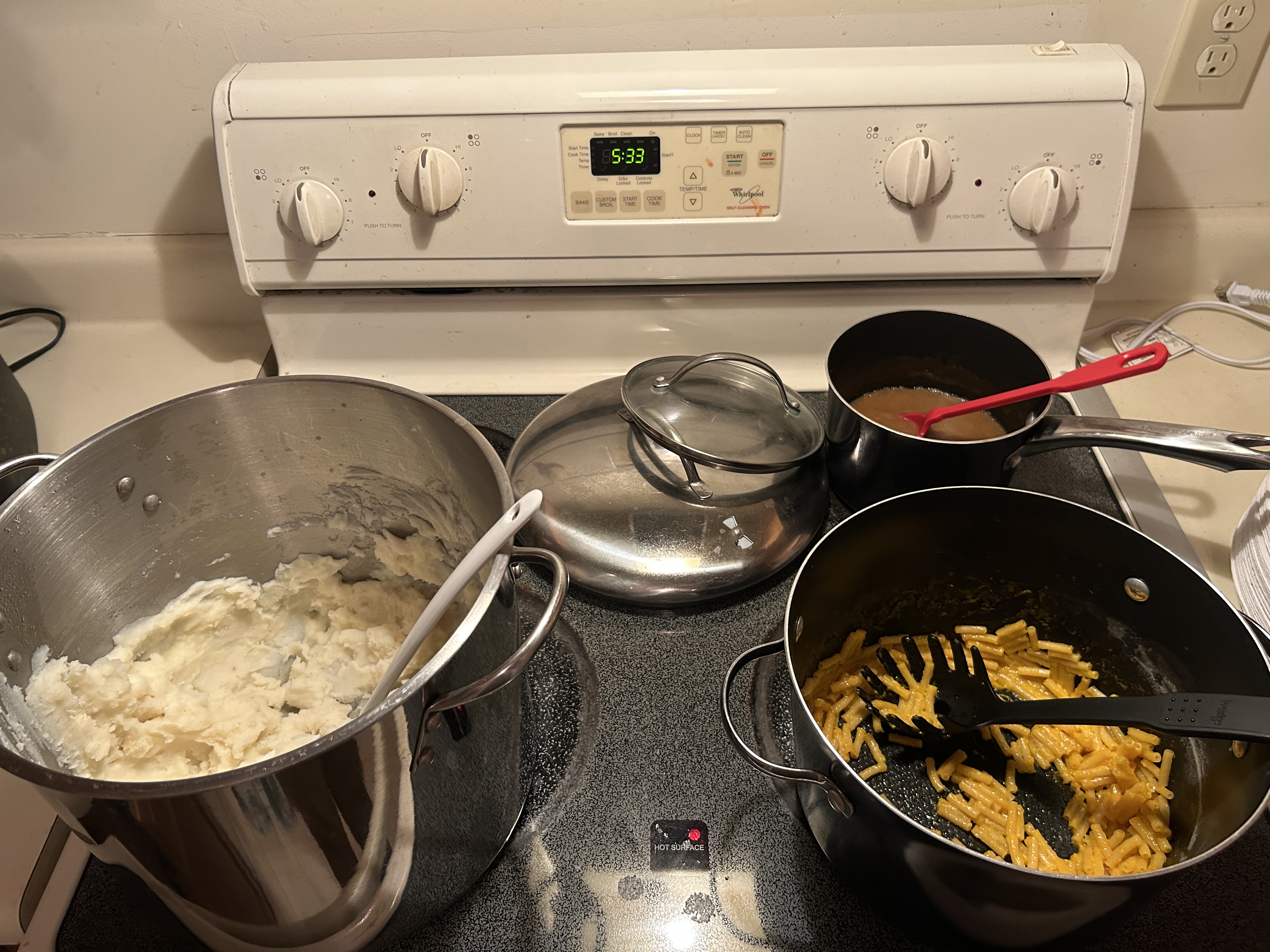 Mashed potatoes, mac n cheese, and gravy in pots on a stovetop.